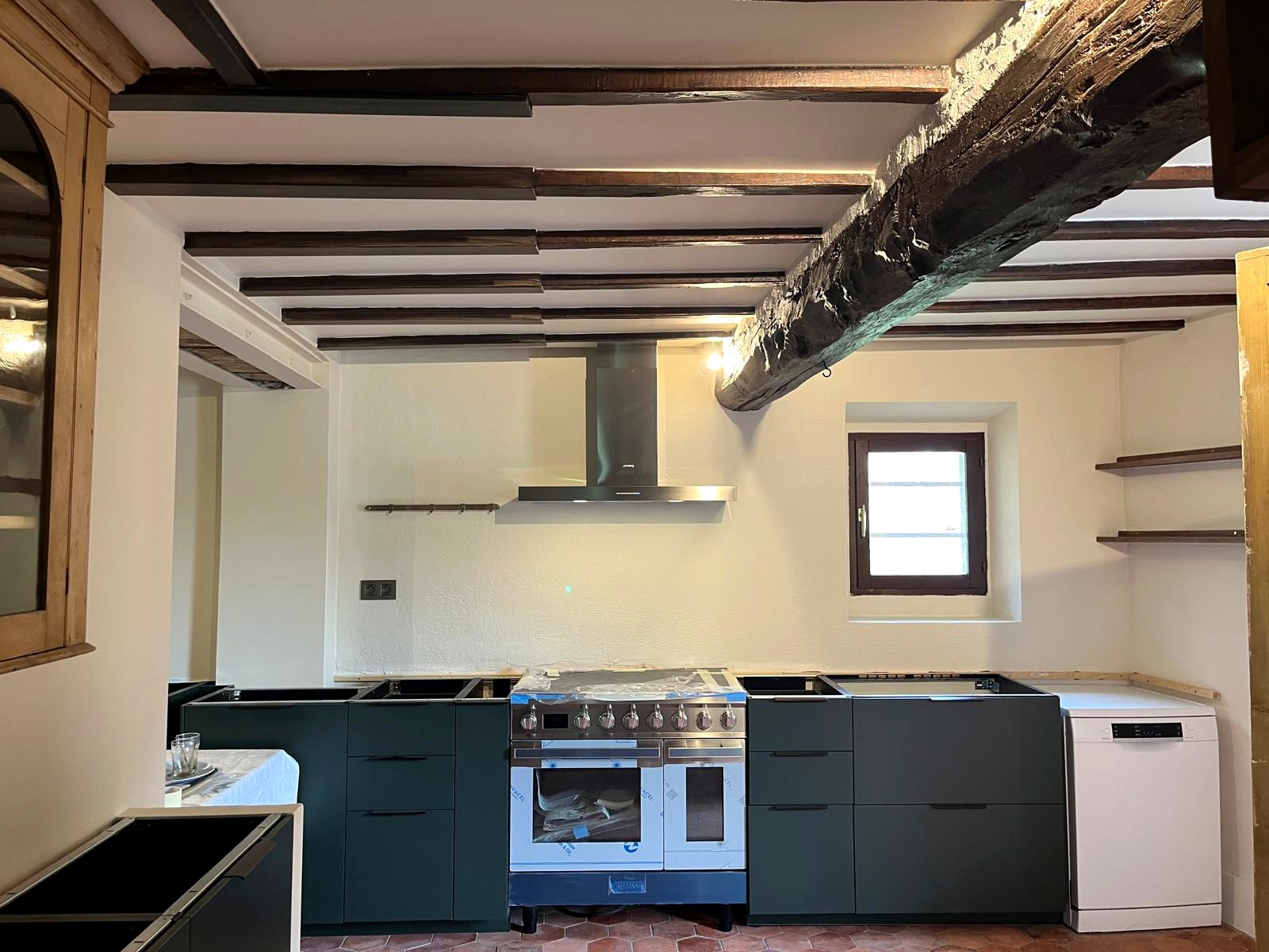 Cuisine aux meubles foncés sous poutres apparentes, plan de travail encore en cours de pose — chantier CAREN