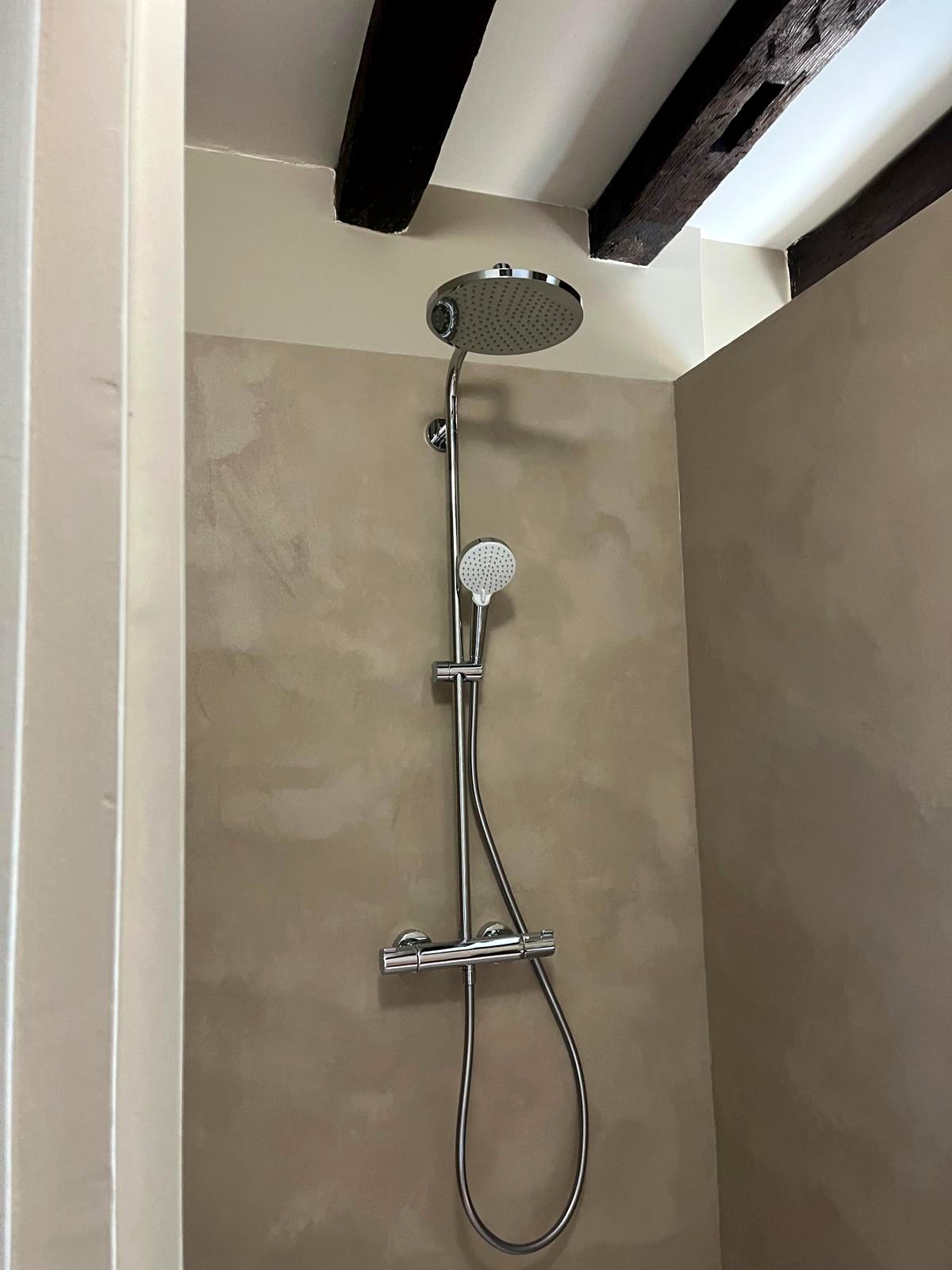 Colonne de douche chromée sur carrelage clair sous poutres apparentes — chantier CAREN